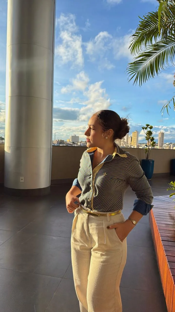 Retrato de Maria Fernanda em terraço urbano, ao entardecer, com a cidade ao fundo.